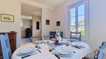 A dining area with a round table set for four, a bottle of wine, and framed pictures on the walls.