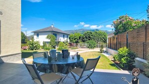 A patio with a round table and chairs, a house in the background, and a clear blue sky. - The Pyrenean Stopover • Between Lourdes and Cauterets. (Argelès-Gazost)