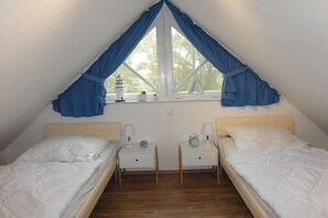 Ein Zimmer mit zwei Betten, einem Fenster mit blauen Vorhängen, einem kleinen Tisch mit einer Lampe und einer Uhr.
