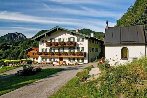 A multi-story building with balconies, a separate annex, and a gravel path leading to a seating area. - Alpenrose Leitnerhof (Bad Reichenhall)