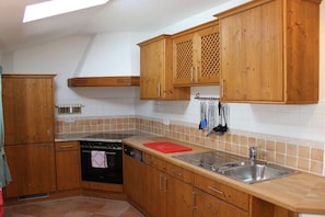 A kitchen with wooden cabinets, a stove, a dishwasher, and a sink. - Alpenrose Leitnerhof (Bad Reichenhall)