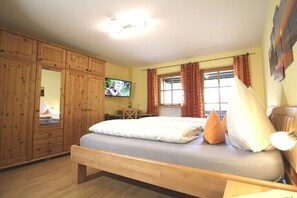 A bedroom with a bed, wooden wardrobe, television, window with curtains, and a desk with a chair. - Alpenrose Leitnerhof (Bad Reichenhall)