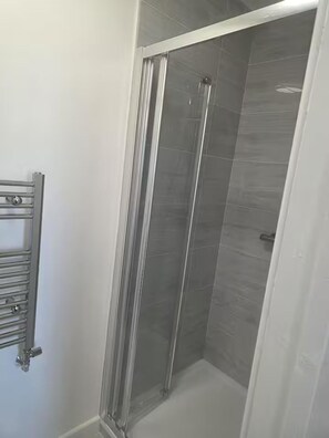 Una ducha con puerta de cristal y un perchero de metal.