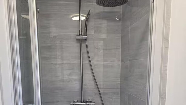 A walk-in shower with a glass door, a handheld showerhead, and a wall-mounted control panel. - House Sleeps 7 With Garden and Parking (Erith)