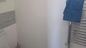 A bathroom with a toilet, a towel rack with a blue towel, and a mirror. - House Sleeps 7 With Garden and Parking (Erith)