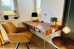 Ein moderner Arbeitsplatz mit Schreibtisch aus Holz, einem Stuhl, einer Lampe, einer Topfpflanze und einer Pendelleuchte.