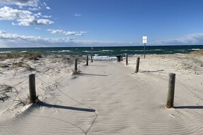 Ein Sandweg am Strand, der zum Meer führt, mit einem Wegweiser und Holzpfählen.