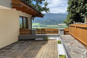 Eine Holzterrasse mit Steinbelag, ein Holenzaun und Blick auf eine gebirgige Landschaft.