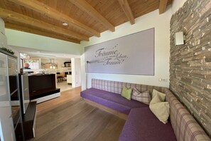 Ein Wohnzimmer mit Steinsturz, großem Flachbildfernseher, violettem Sofa und Holzboden.