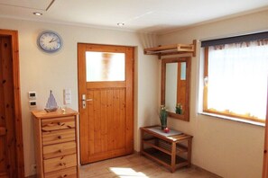 Ein Zimmer mit Holztür, einem Schminktisch, einem Spiegel und einem Fenster mit Vorhängen.