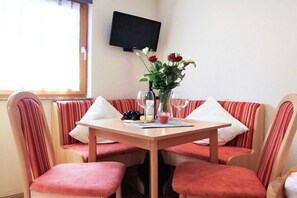 Ein Essbereich mit Tisch, Stühlen, einer Blumenvase und einem Fernseher an der Wand.