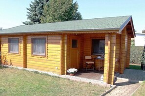 Eine kleine Holzhütte mit Veranda, zwei Fenstern und einem Tisch mit Stuhl.