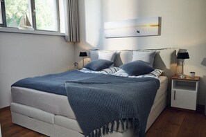 Ein Schlafzimmer mit einem Bett, Nachttischen, einem Fenster und einem Wandbild.