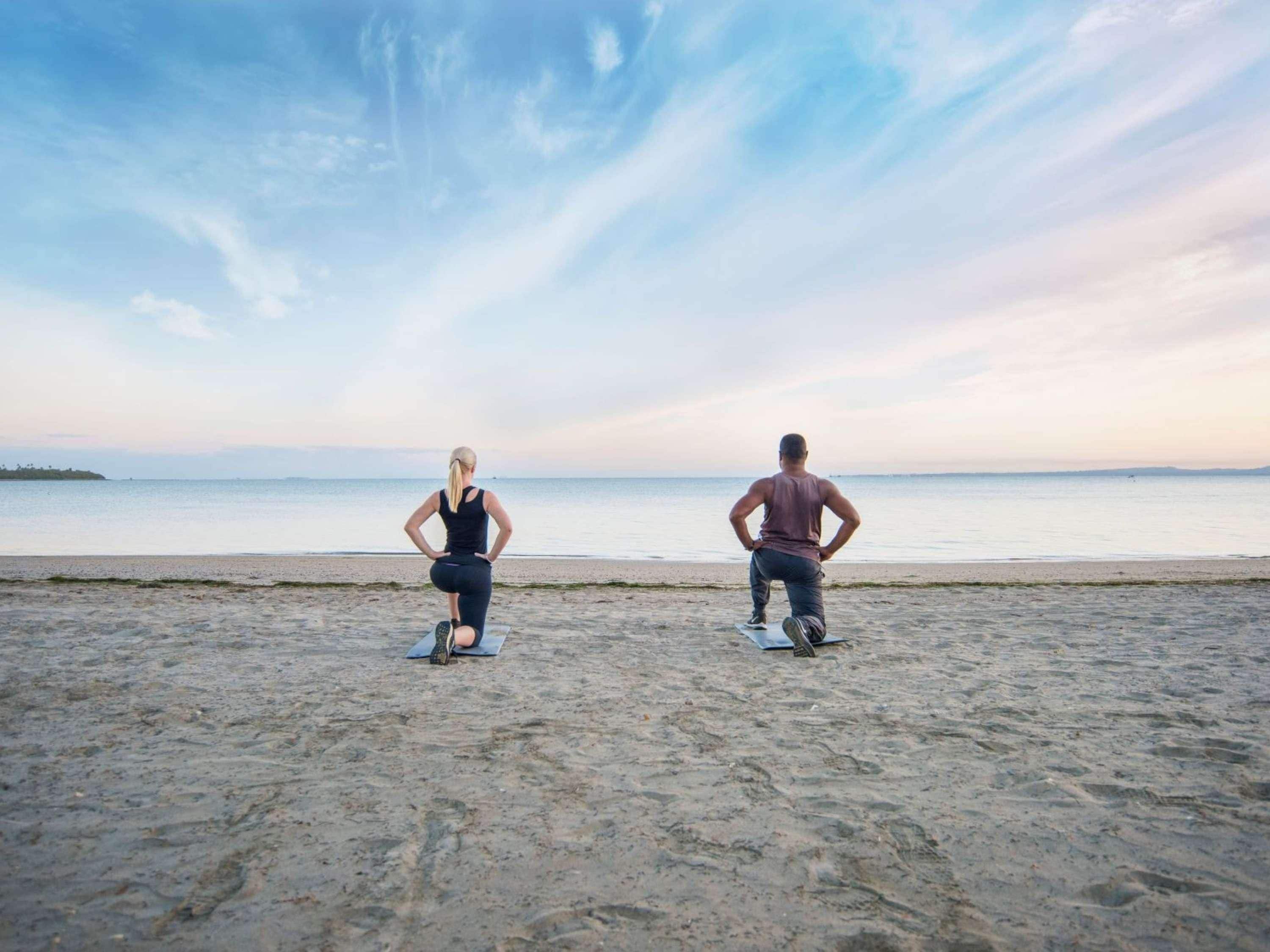 Two individuals exercising on a sandy beach with a calm sea and a clear sky in the background.