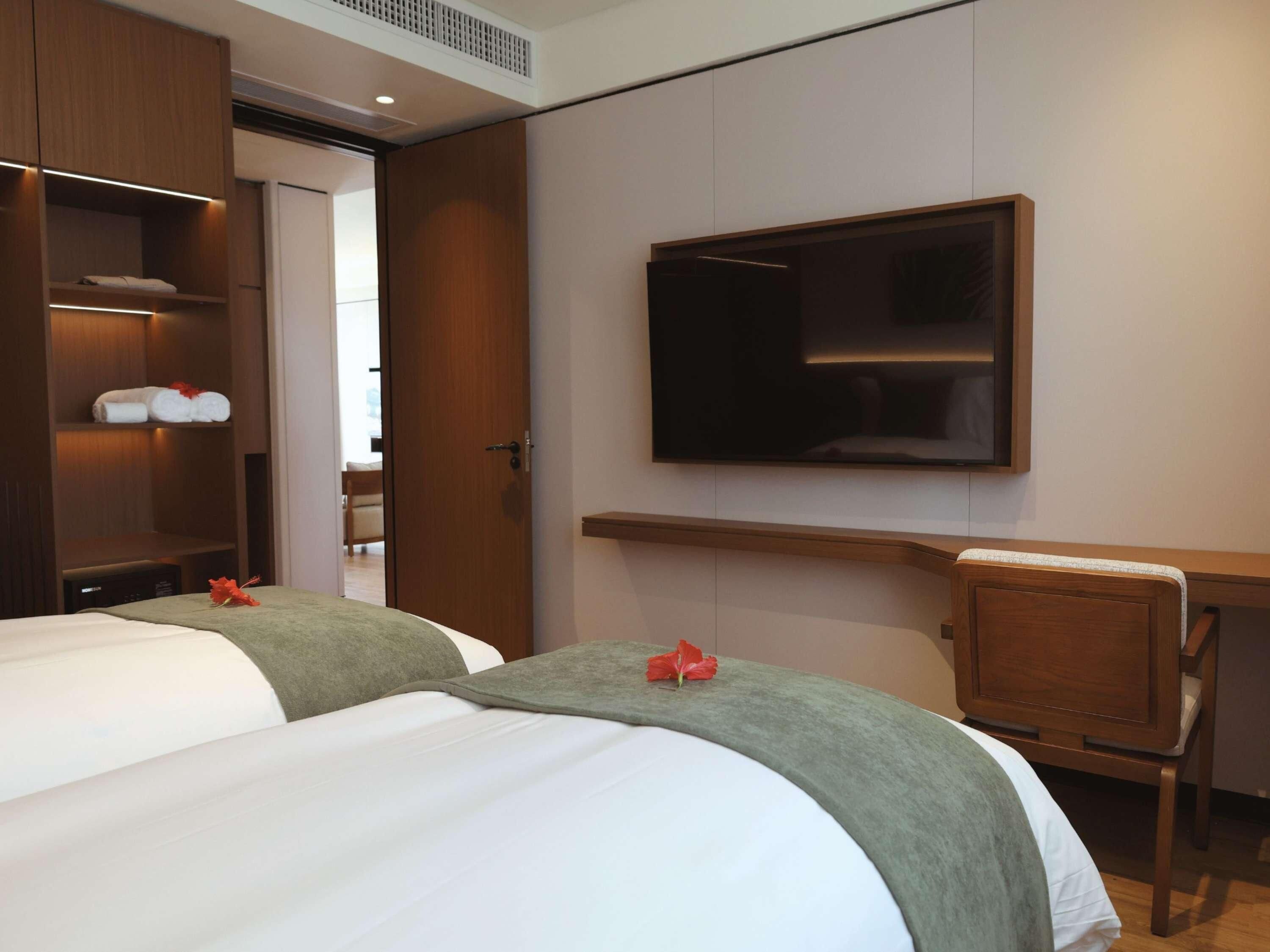 Ein Hotelzimmer mit zwei Betten, einem Schreibtisch und einem an der Wand befestigten Fernseher.