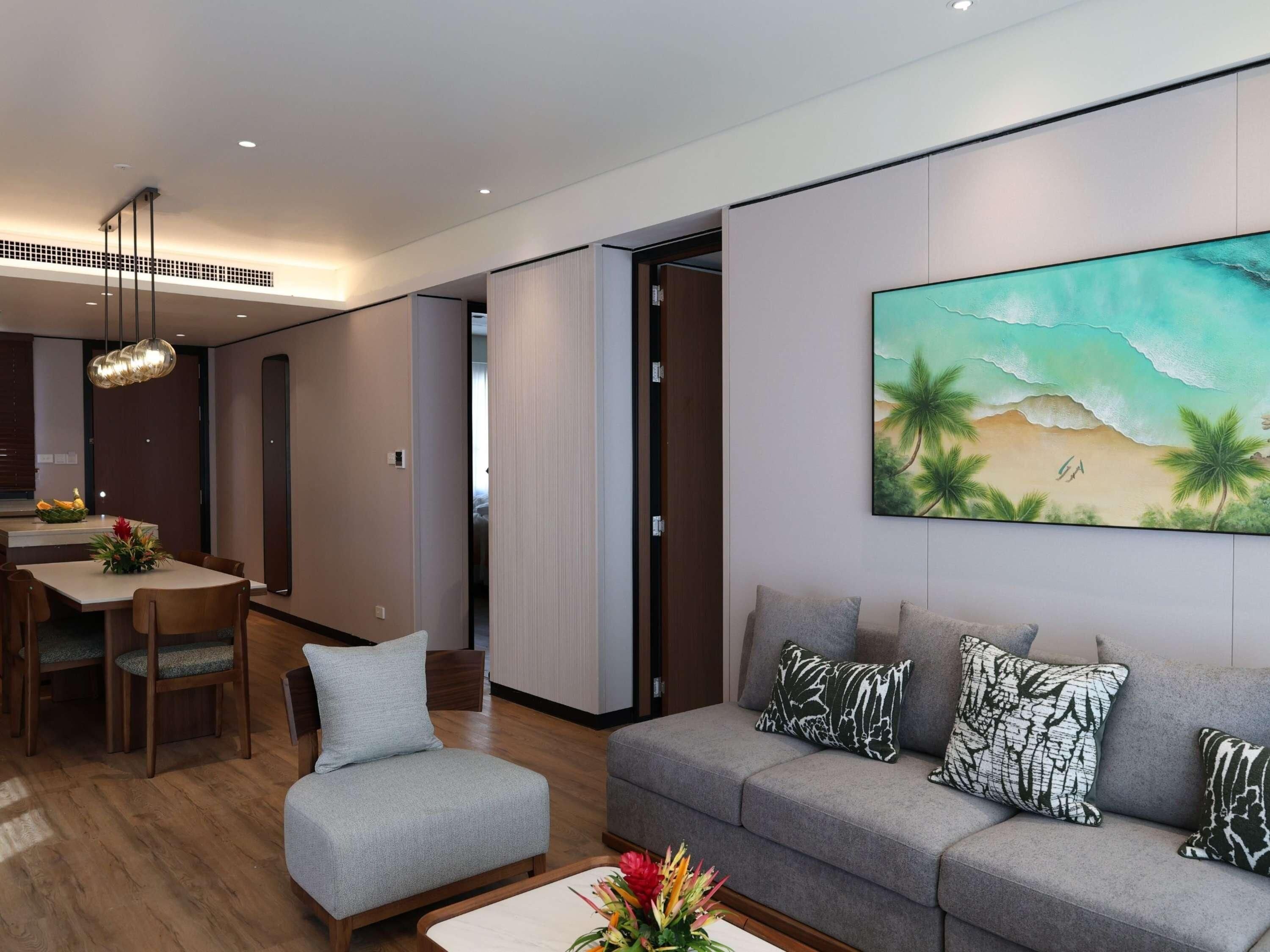 Un salon moderne avec un canapé gris, un coin repas comprenant une table et des chaises, et un grand tableau mural représentant une scène de plage.