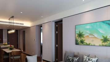 Un salon moderne avec un canapé gris, un coin repas comprenant une table et des chaises, et un grand tableau mural représentant une scène de plage.