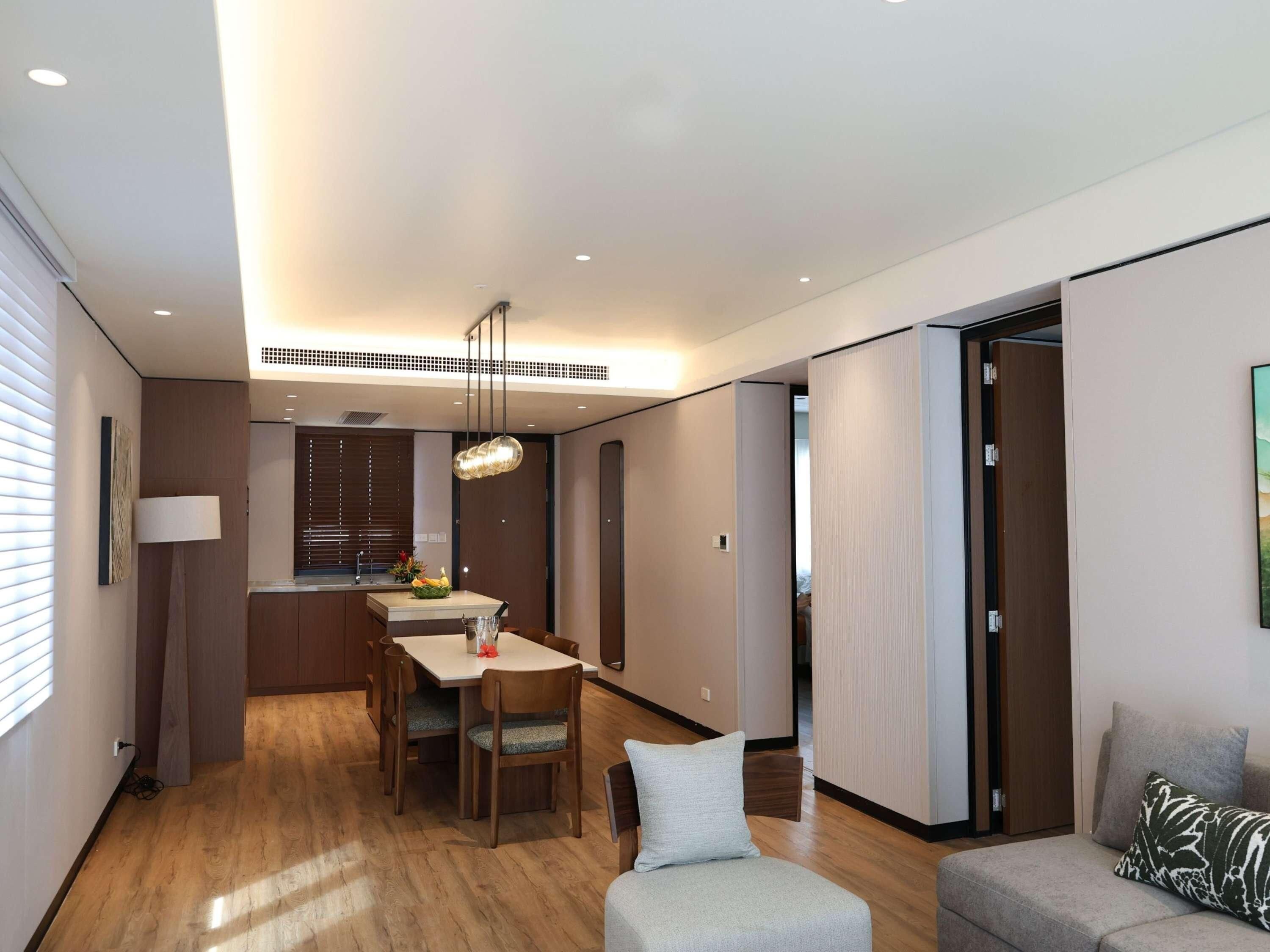 A modern living room with a dining area, wooden flooring, and a ceiling with recessed lighting.