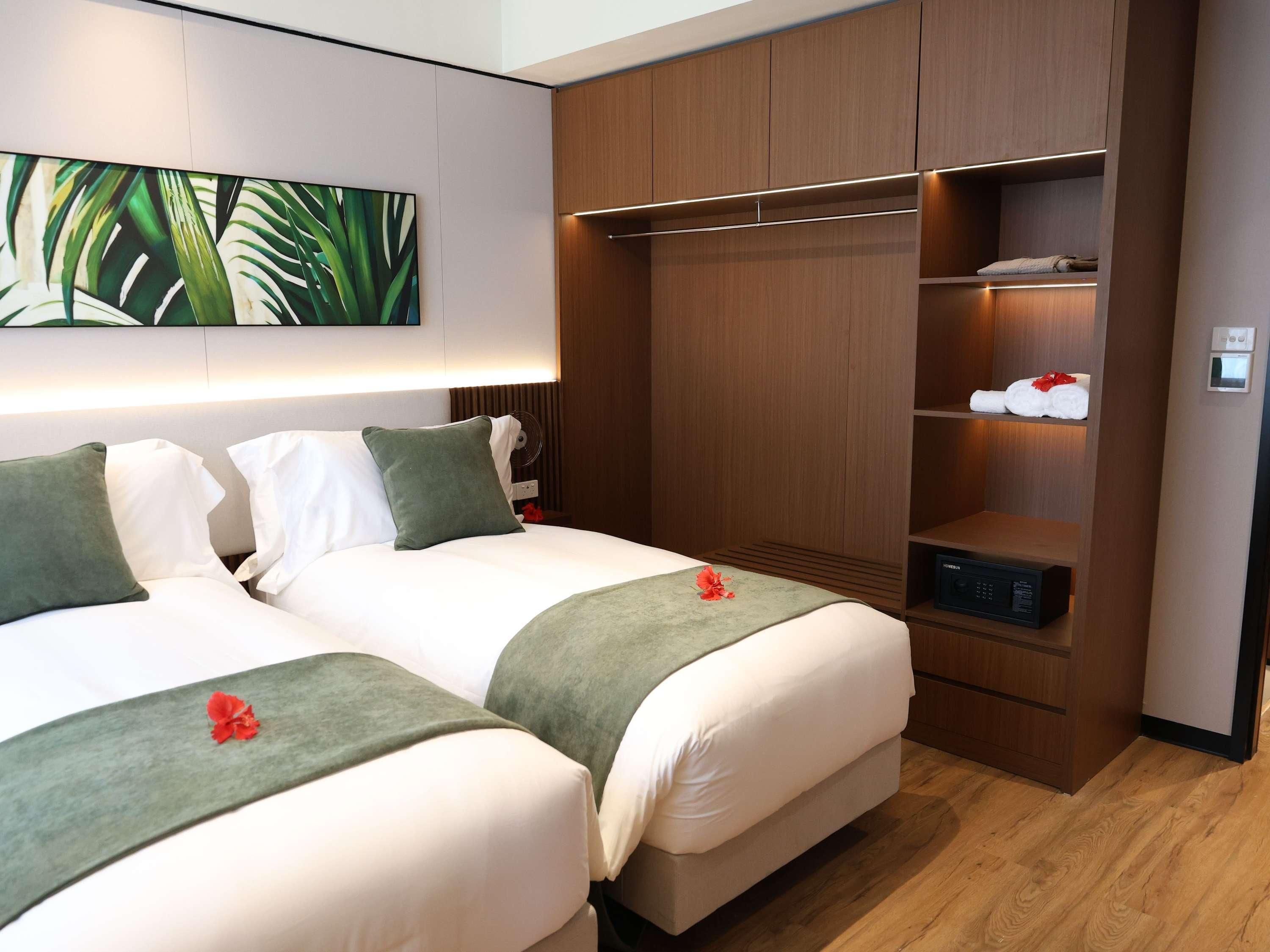 A hotel room with two beds, a large artwork on the wall, a wooden wardrobe, and a small shelf with towels.