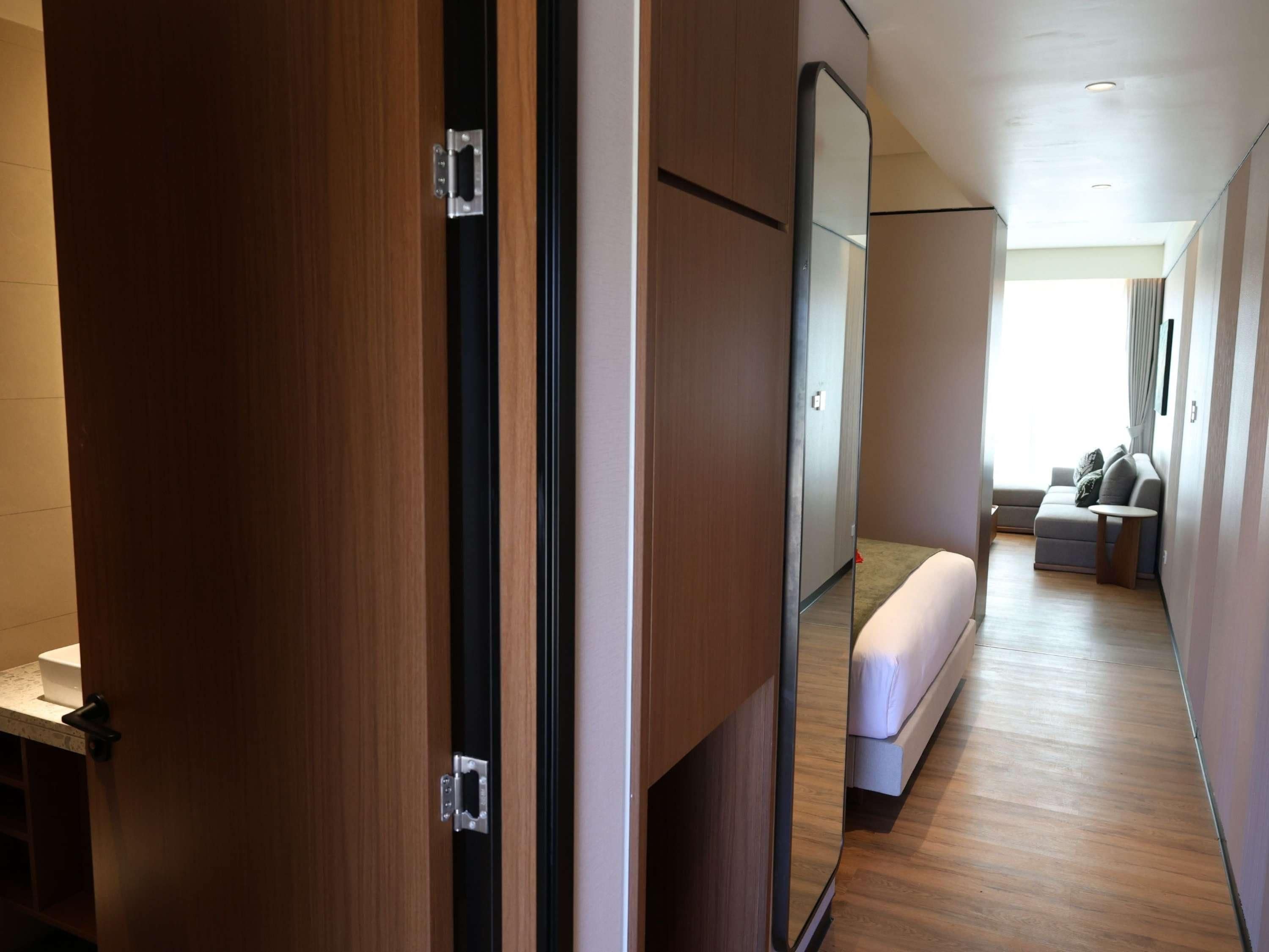 Een hotelkamer met houten vloer, een bed, een zithoek met een bank en een kleine tafel, en een grote spiegel.