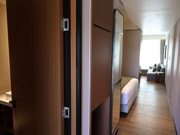Habitación de hotel con piso de madera, una cama, zona de estar con sofá y una mesita, y un espejo grande.