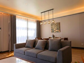 Una sala de estar moderna con un sofá gris, un comedor con mesa y sillas, y un amplio ventanal con cortinas.