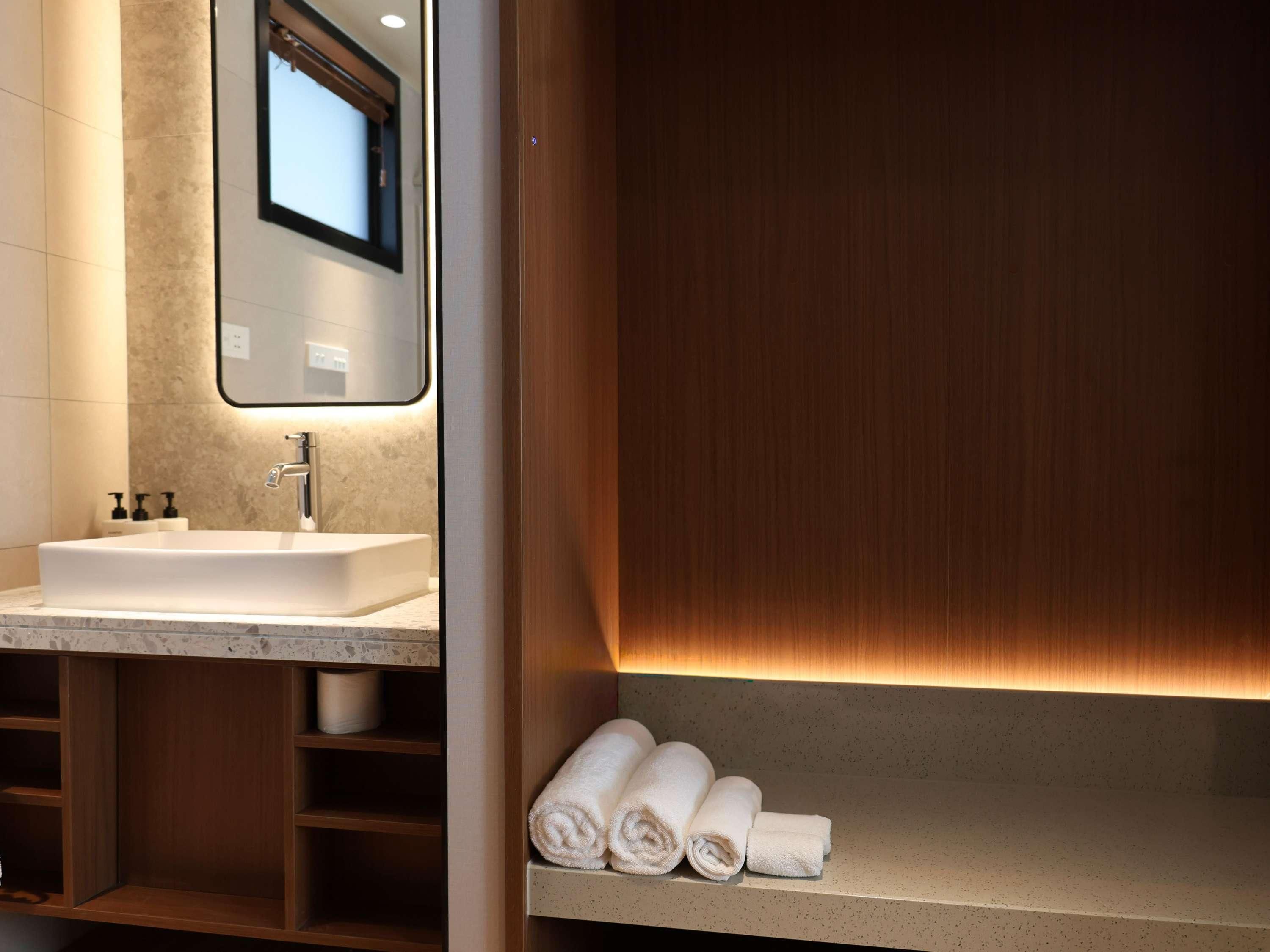 A modern bathroom with a white sink, a mirror, and wooden shelves.