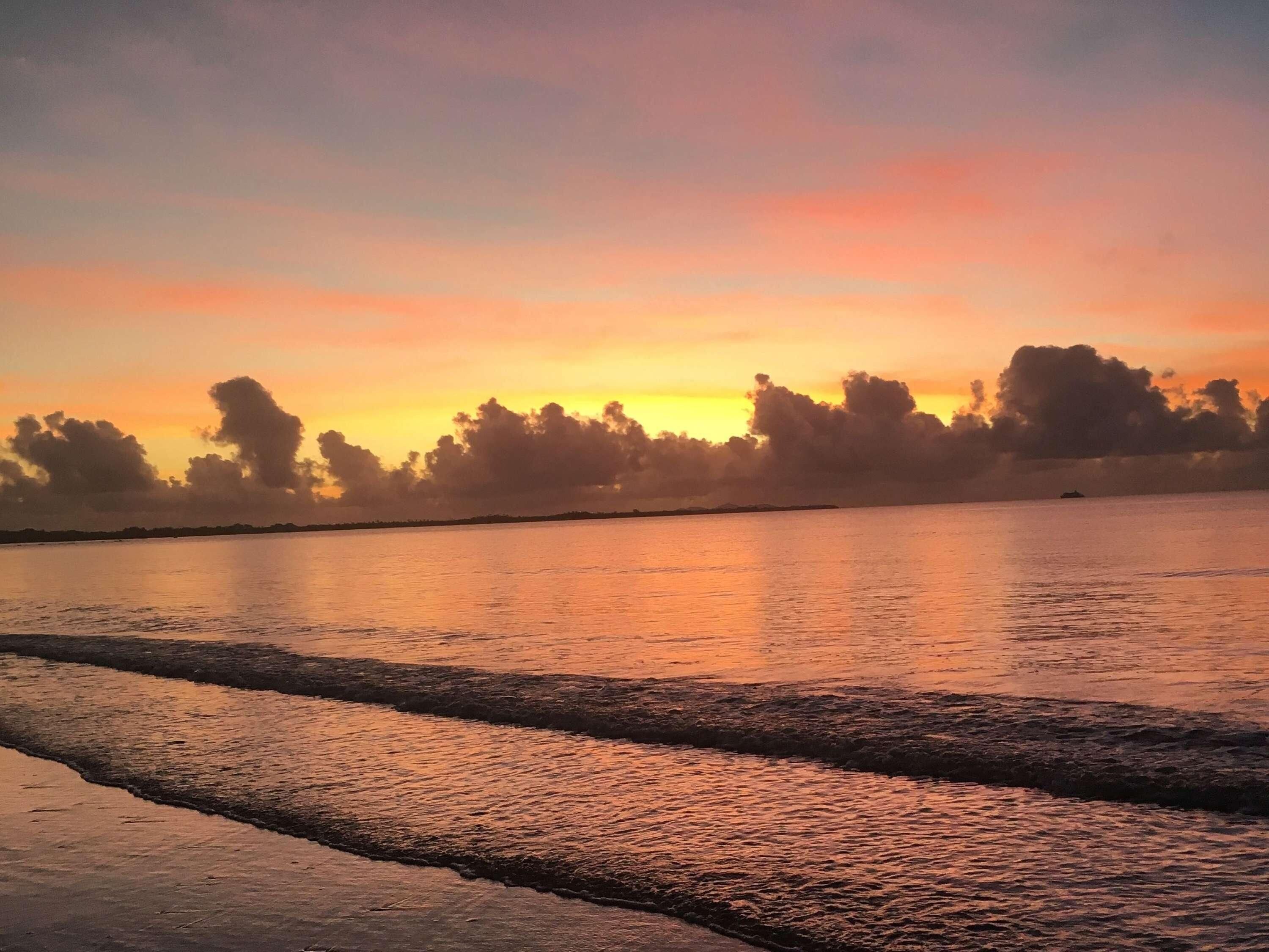 Ein Sonnenuntergang über ruhigem Wasser mit einer entfernten Küstenlinie.
