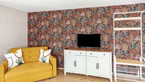 A living room with a sofa, TV, white cabinet, and a patterned wall. - Apartment "Harmonie Oasis" with Wi-Fi and Air Conditioning (Alsleben)