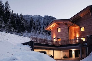 Ein modernes Holzhaus mit Balkon, umgeben von schneebedeckten Bäumen.