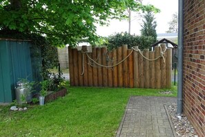 Ein umzäunter Garten mit einem Ziegelweg, einem Metallfass und einem grünen Schuppen.