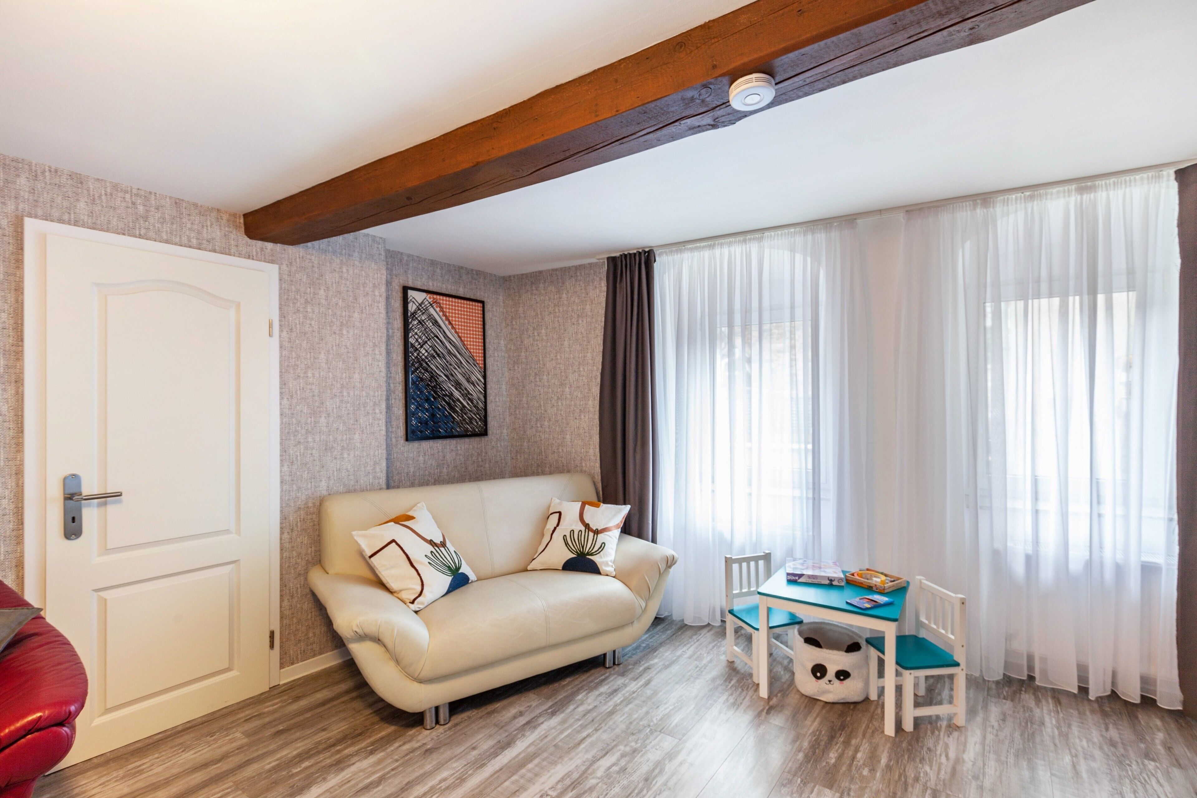 Una sala de estar con sofá, una mesa de comedor con sillas, una puerta y una ventana con cortinas.