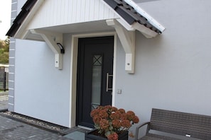 Ein weißes Gebäude mit einer schwarzen Tür, einer kleinen Veranda und einer Bank.