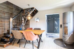 A modern kitchen with a built-in stove, a dining area with a wooden table and chairs, and a staircase with a metal railing. - Holiday home in Aurich with swimming pool (Aurich)