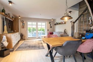 A modern kitchen with a wooden dining table, grey chairs, and a hanging light fixture. - Holiday home in Aurich with swimming pool (Aurich)