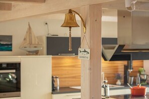 Eine Küche mit Holzbalken, einer hängenden Messingglocke und einem Schild mit der Aufschrift 'KOMBÜSE'.