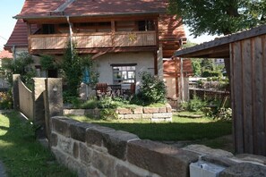Une maison en bois à deux étages, dotée d’un balcon, d’un mur en pierre et d’un jardin.
