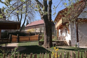 Ein rustikales Gebäude mit Steinaußenwand, einer Holzdar Terrasse und einem großen Baum im Vordergrund.