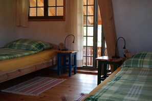 Ein Zimmer mit zwei Betten, einem Fenster, einer Tür und einem kleinen Hocker.
