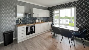 Una cuina moderna amb armaris blancs, un taulell de fusta i una zona de menjador amb dues cadires.