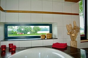 Ein modernes Badezimmer mit einer Badewanne, einem Fenster mit Ausblick und einer Vase mit Trockenblumen.