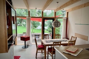 Ein Essbereich mit Tisch, Stühlen und Blick auf einen Garten durch große Fenster.
