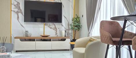 Un salón moderno con una pared de mármol, un televisor de pantalla plana, una mesa de centro redonda y un sofá color beige.