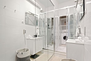 Ein modernes Badezimmer mit einer Duschkabine, einer Waschmaschine und einem Waschbecken mit Spiegel.