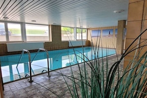 Ein Innenpool mit großen Glaswänden, Metallleiter und Fliesenboden.