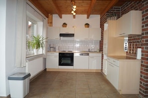 A kitchen with white cabinets, a black oven, a dishwasher, and a window with a plant. - Holiday home with 1 bedroom (Butjadingen \/ Burhave)