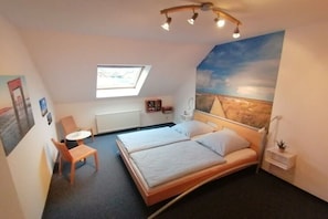 A bedroom with a bed, a desk, a chair, a small table, a radiator, a window, and a wall mural. - Holiday home with 1 bedroom (Butjadingen \/ Burhave)