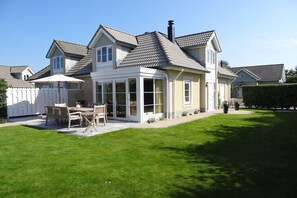 Ein zweigeschossiges Haus mit überdachter Terrasse, einem eingezäunten Garten und einem gepflegten Rasen.