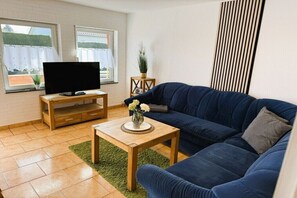 A living room with a blue sofa, a wooden coffee table, a TV on a wooden stand, and a potted plant. - with boat/ house Haveleck (Ketzin\/Havel)