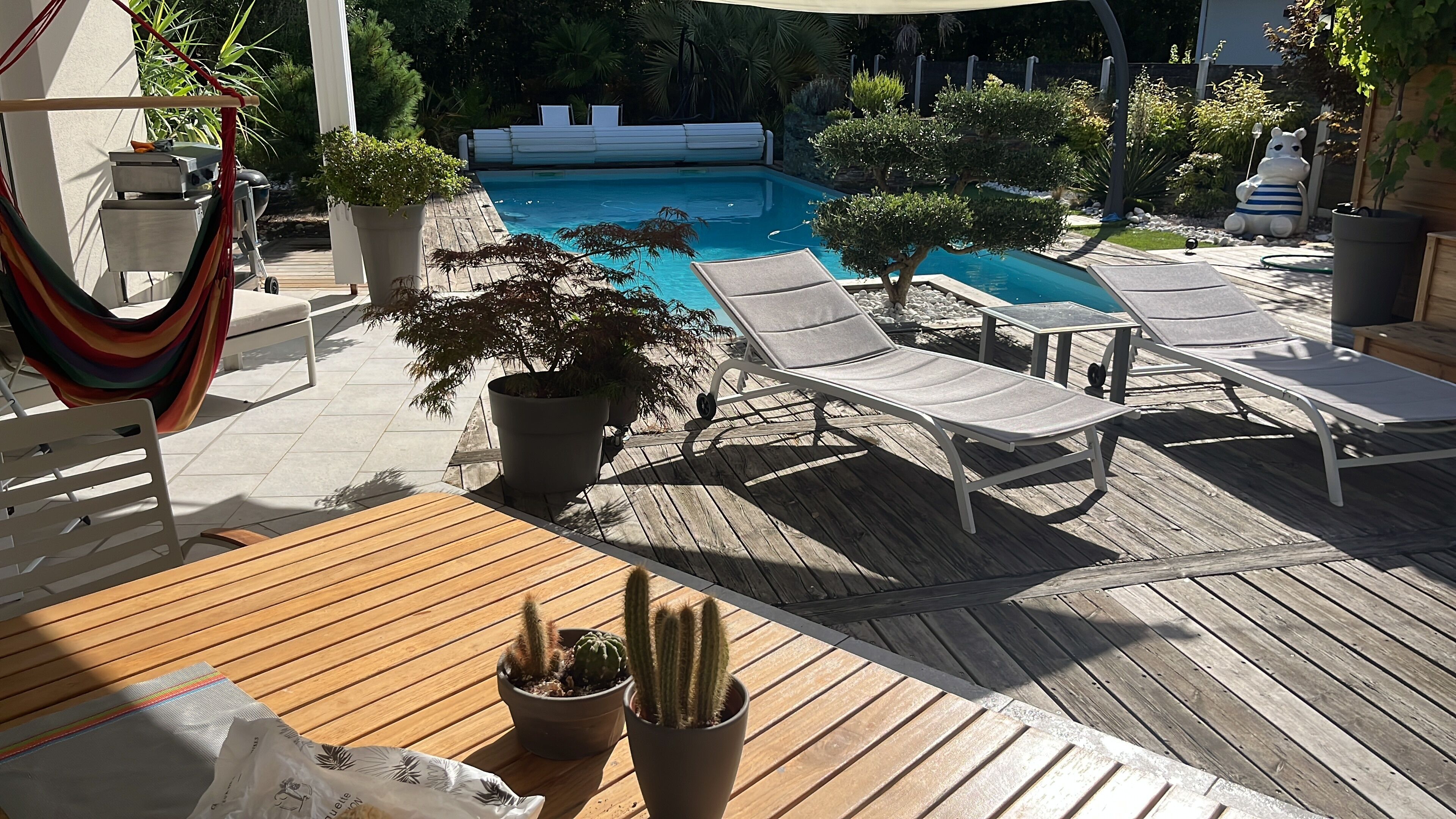 A wooden deck with lounge chairs, a pool, and potted plants.